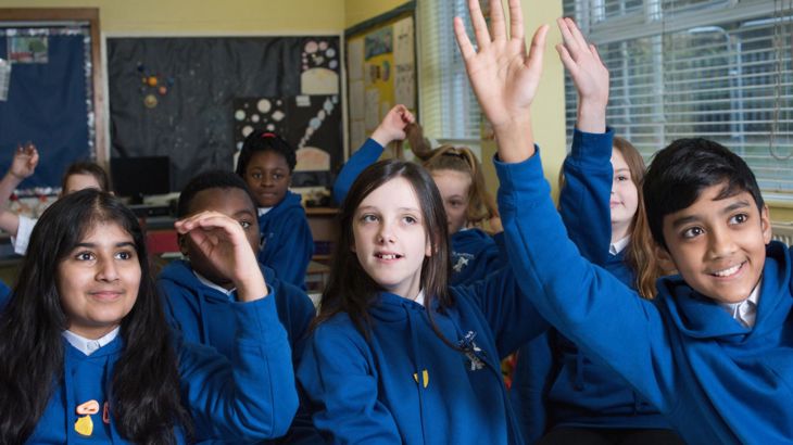 pupils in classroom raising their hands