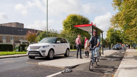 Man on bicycle on protected cycle lane, passing a bus stop
