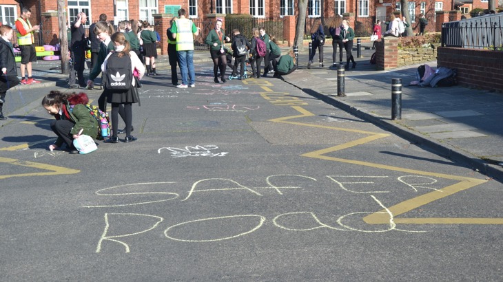 road outside school is closed to cars and children are playing and drawing with chalk