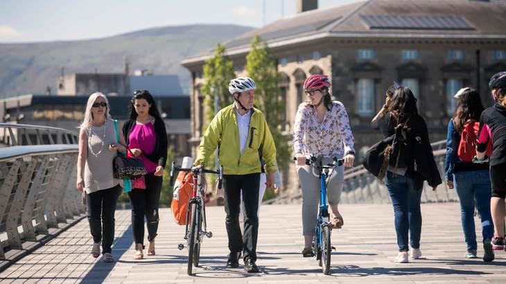 People walking and on bikes crossing bridge in urban setting