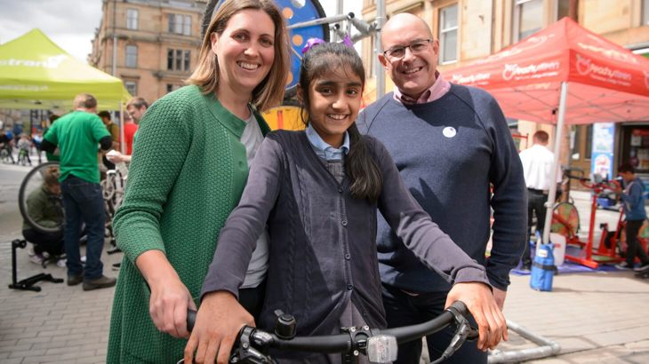 Walk Wheel Cycle Trust in Scotland Director John Lauder with a member of the community and a school child on a bicycle at a street event