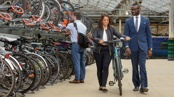 man and woman pushing bike at train station bike storage facility