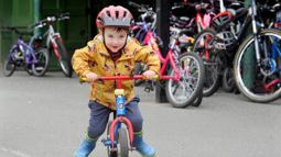 Toddler with helmet and yellow coat on, riding a red bicycle