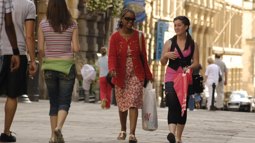 Two female friends walking through high street with others walking in the background
