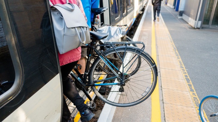 Bike being carried by person with blue backpack from train platform onto train