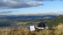 Someone sitting on grassy hillside with bike behind them, looking out on Welsh valley with quarry below