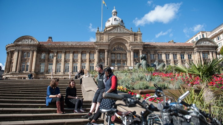 A group of people sit outside Birmingham Council building on a sunny day