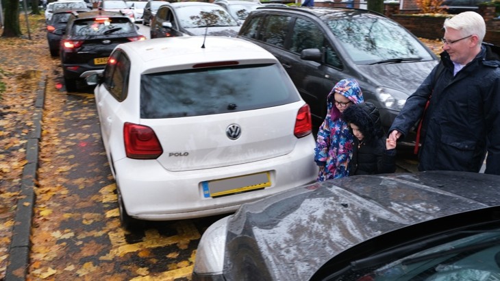 A parent walks a child inbetween cars outside of a school 