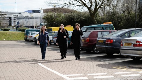 Three women walk through a car park in an industrial setting