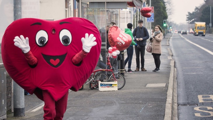 Walk Wheel Cycle Trust heart-shaped air quality mascot stands at a bus stop. 