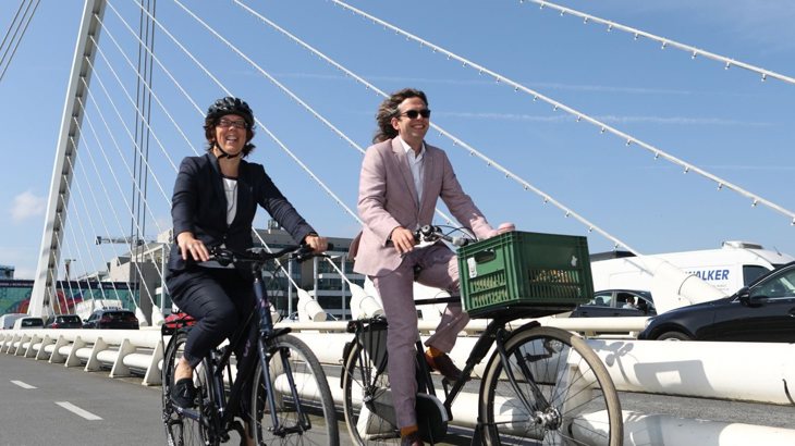 Anne Graham CEO National Transport Authority and Xavier Bryce CEO Walk Wheel Cycle Trust cycling on two bikes across bridge in Dublin 