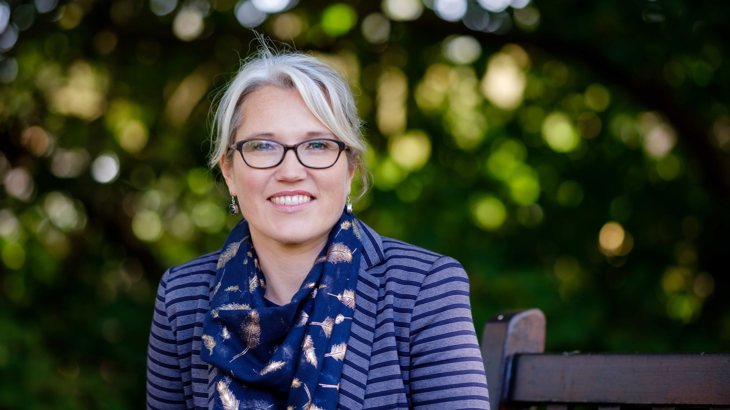Head shot of Christine Boston, Walk Wheel Cycle Trust in Wales director, wearing glasses, a striped purple top and a navy scarf, smiling with greenery in the background.