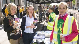 staff member dianne at an information stand with two women holding cycling literature at cycle to work day event outside in Belfast City Centre