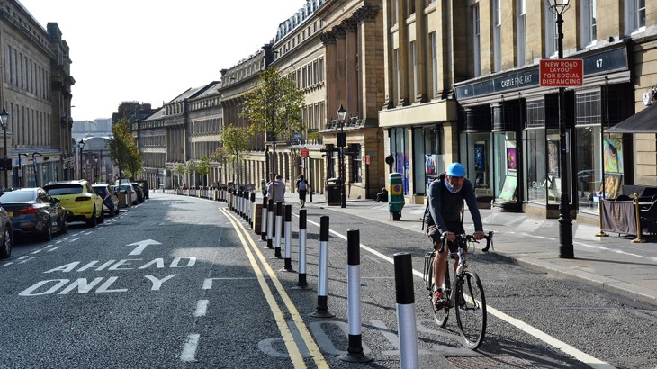 A man wearing a cycle helmet riding uphill along a segregated cycle lane through a city centre.
