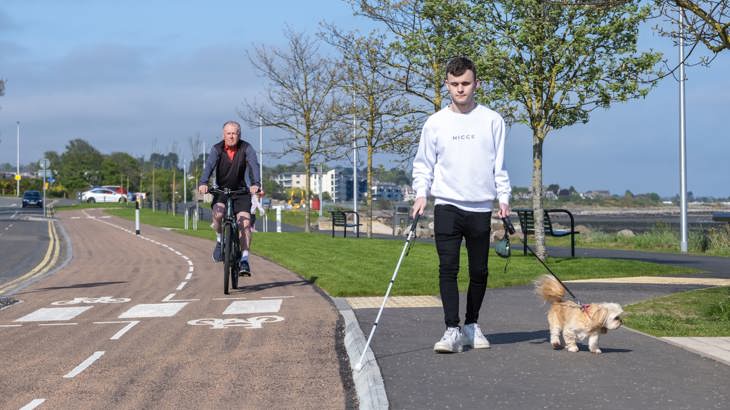 Elderly Male Cyclist And Visually Impaired Man Walking Dog