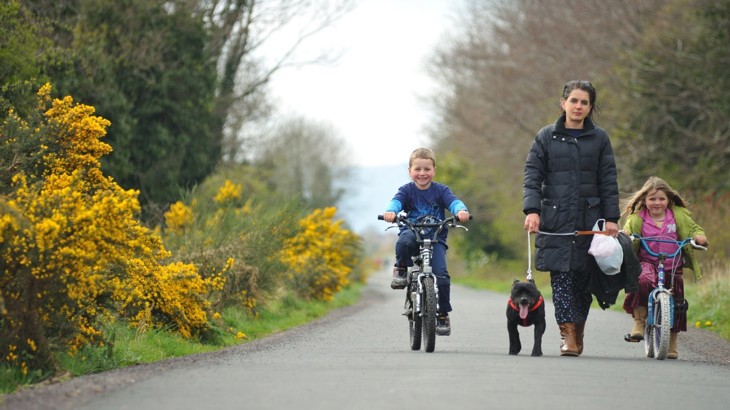 Young boy and girl cycling on cycle path with woman walking a dog