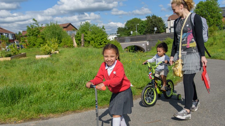 Girl on scooter, boy on bike and mum walking to school along a traffic-free path