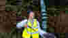 A woman in high-vis standing in front of a milepost on the Network smiling while litter picking 
