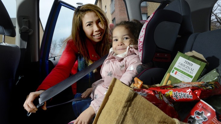 A mum fastens her daughter's seat belt in the car after going shopping