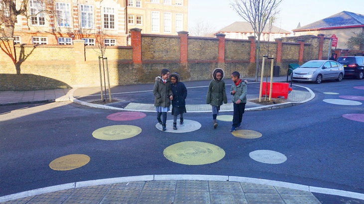 Children walking and cycling across a newly pedestrianised street with colourful drawings on ground outside school