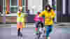 A woman in a bright yellow jacket pushing a bike across the road in front of a lollypop lady with a small child sat on a seat at the back of the bike