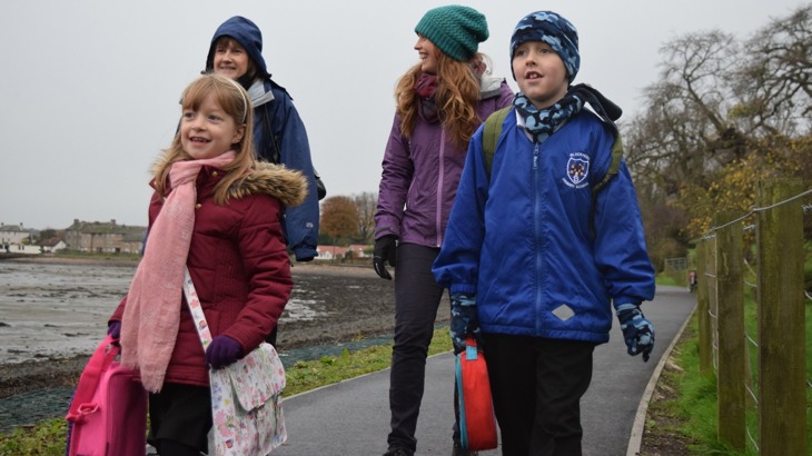 Two women and two children walk to school. They are wrapped up warm.