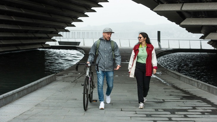 Man holding a bike walking with a woman in Dundee, with the V&A building in the background