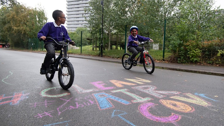 Two school boys cycling in playground with "Clean Air" written in chalk on the ground