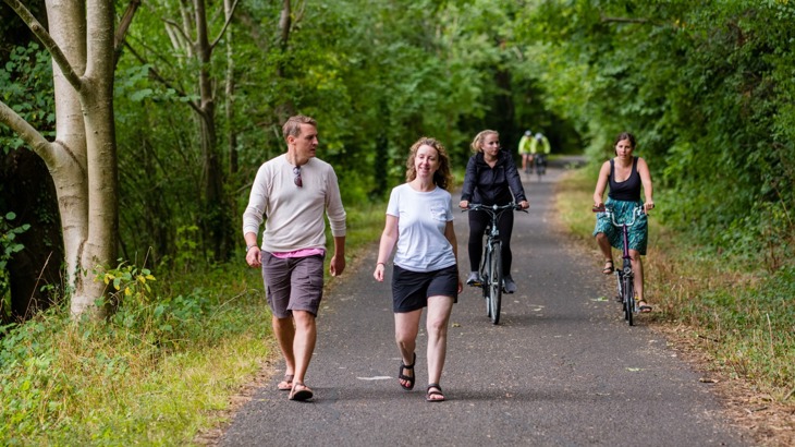 people walking and on bikes using traffic-free path lined with trees