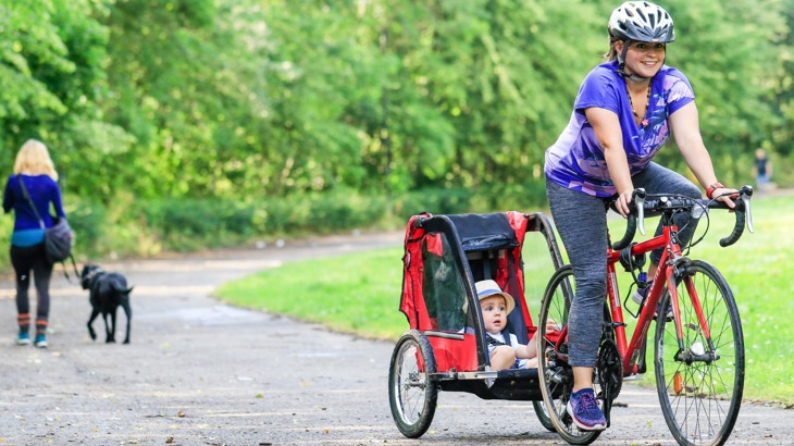 Woman cycling on cycle path pulling small child in trailer